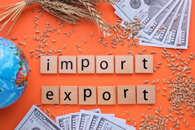 Photo of Words Import and Export made of wooden squares, ears of wheat, banknotes and globe on orange background, flat lay