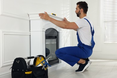 Photo of Professional technician using construction level for installing electric fireplace in room
