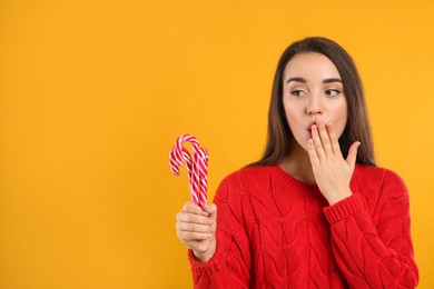 Photo of Young woman in red sweater holding candy canes on yellow background, space for text. Celebrating Christmas