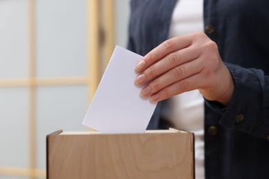 Photo of Woman putting her vote into ballot box on blurred background, closeup