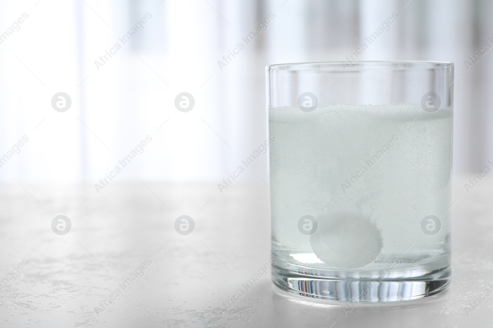 Photo of Glass of water with effervescent tablet on light table indoors, space for text