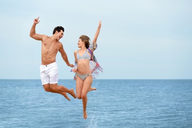 Photo of Happy young couple jumping together on sea beach. Space for text