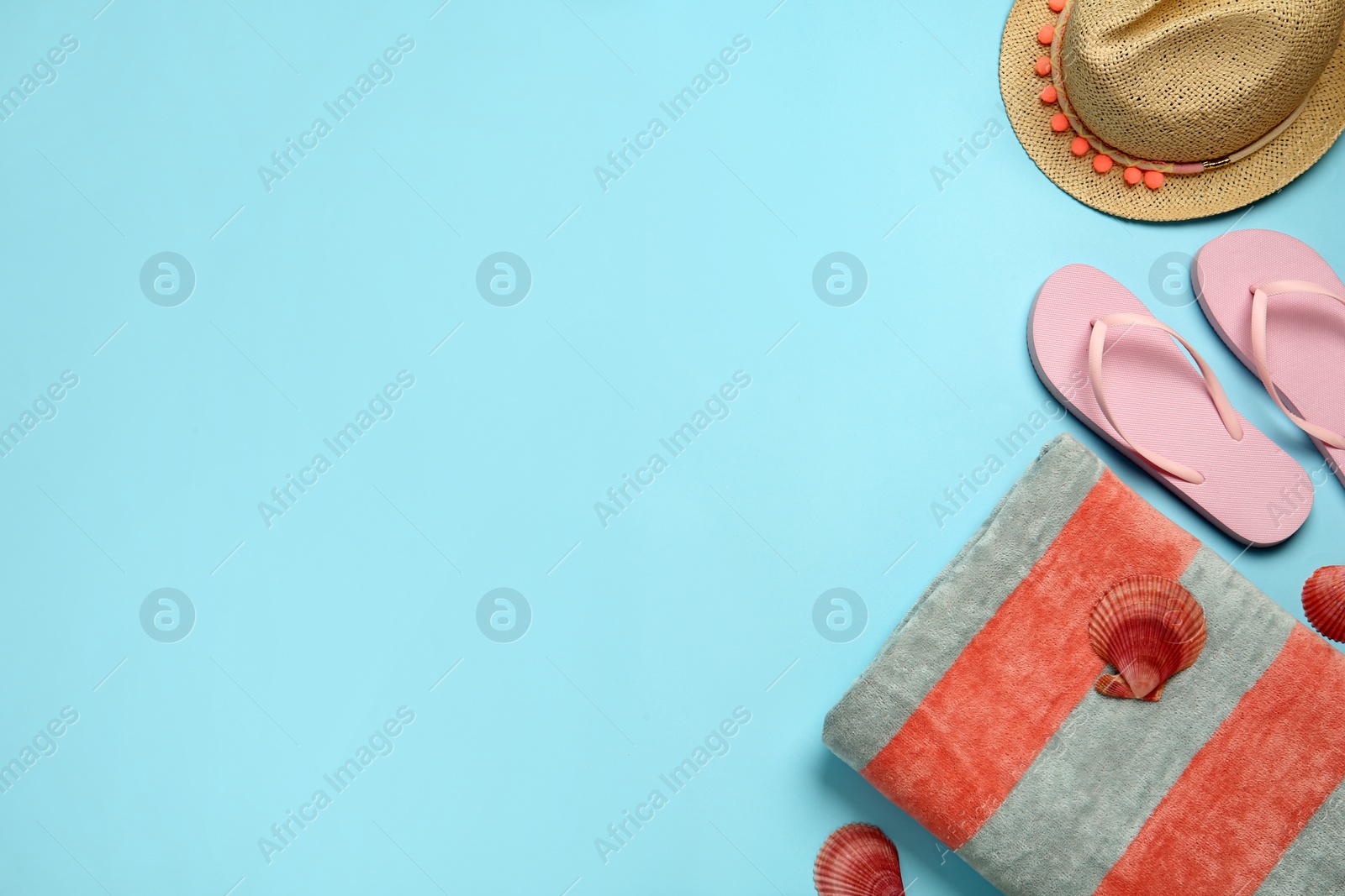 Photo of Beach towel, flip flops and hat on light blue background, flat lay. Space for text