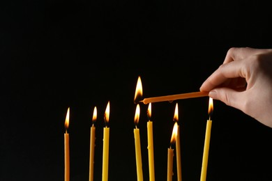 Photo of Woman lighting church candle on black background, closeup