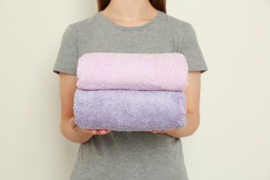 Photo of Woman holding folded soft terry towels on light background, closeup