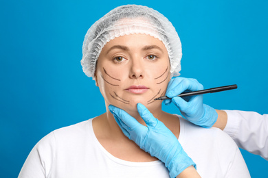 Photo of Doctor drawing marks on woman's face for cosmetic surgery operation against blue background. Double chin problem