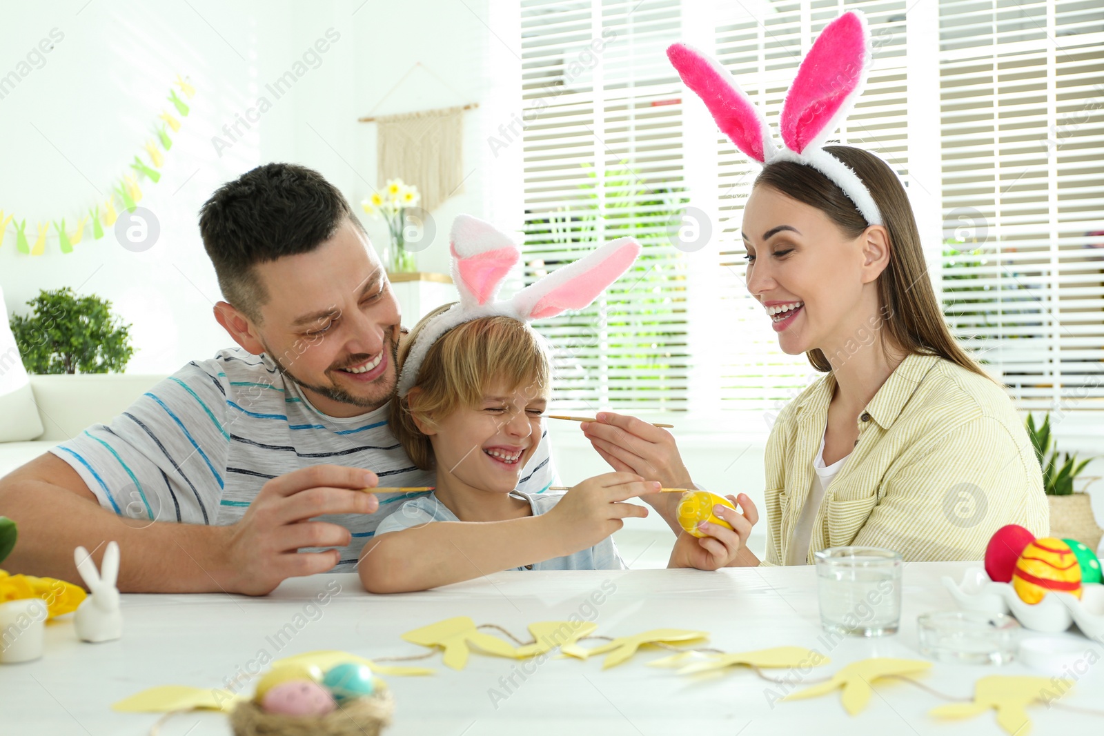 Photo of Happy father, mother and son having fun while painting Easter egg at table indoors