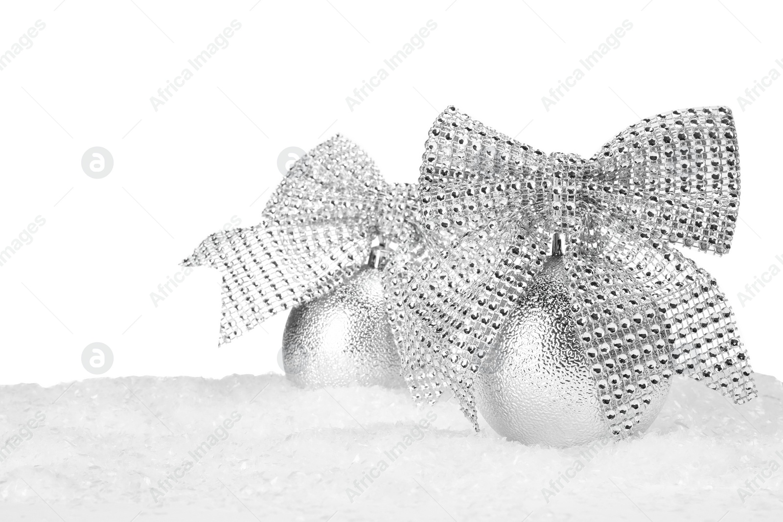 Photo of Beautiful silver Christmas balls with bows on snow against white background