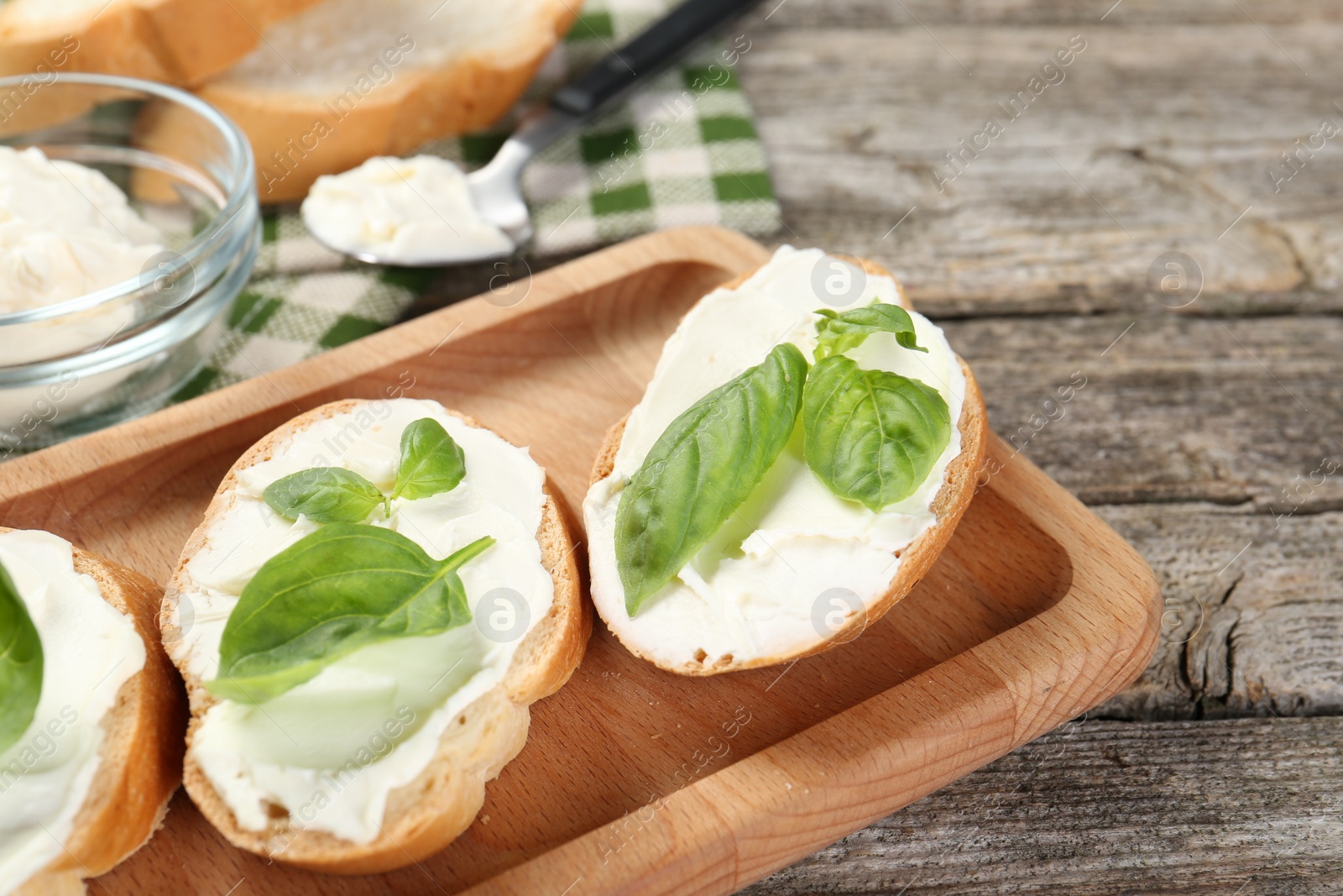 Photo of Delicious sandwiches with cream cheese and basil leaves on wooden table, closeup