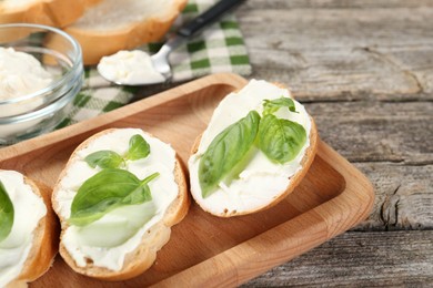 Photo of Delicious sandwiches with cream cheese and basil leaves on wooden table, closeup