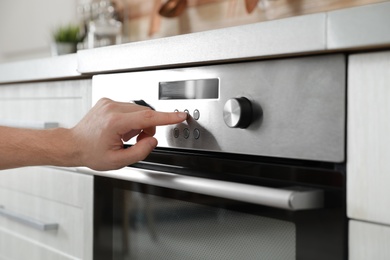 Photo of Man regulating cooking mode on oven panel in kitchen, closeup