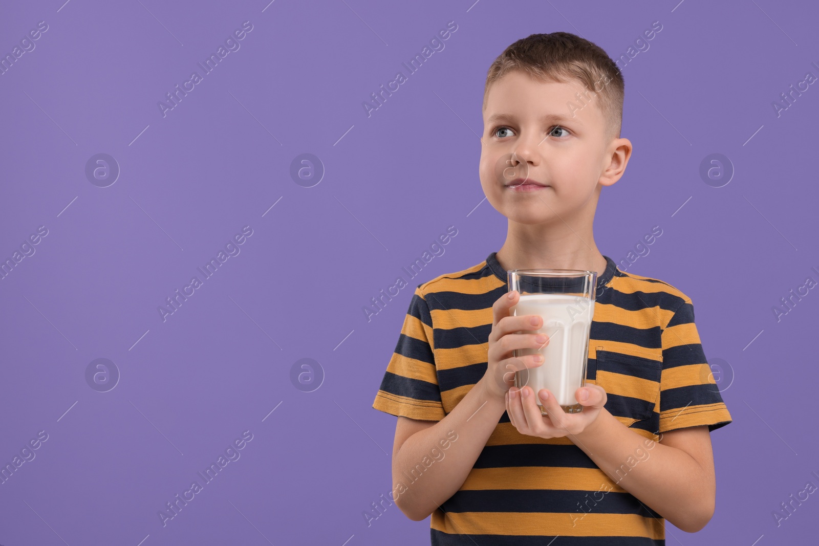 Photo of Cute boy with glass of fresh milk on violet background, space for text