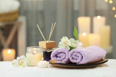 Photo of Beautiful composition with different spa products and flowers on white towel against blurred background