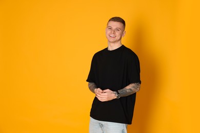 Photo of Smiling young man with tattoos on yellow background. Space for text