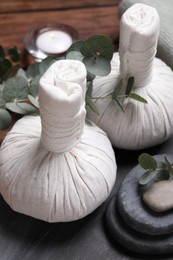 Photo of Beautiful spa composition with herbal massage bags, stones and eucalyptus branches on wooden table, closeup