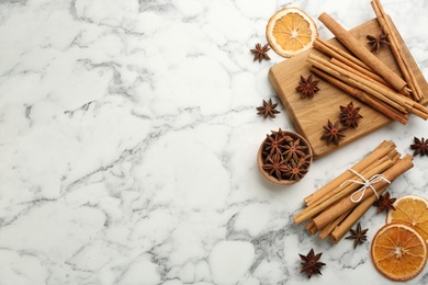 Aromatic cinnamon sticks, dry orange and anise on white marble table, flat lay. Space for text