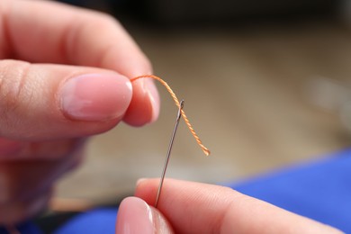 Photo of Woman inserting thread through eye of needle on blurred background, closeup