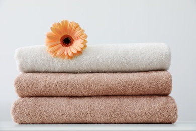 Stack of fresh towels with flower on table against white background