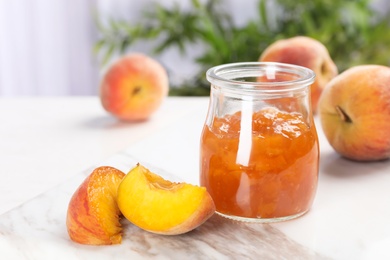 Photo of Jar with tasty peach jam and fresh fruit on table