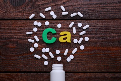 Photo of Paper symbol Ca (Calcium), medical bottle and pills on wooden table, top view