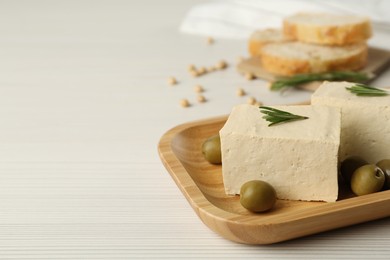 Photo of Pieces of delicious tofu with rosemary and olives on white wooden table, closeup. Space for text