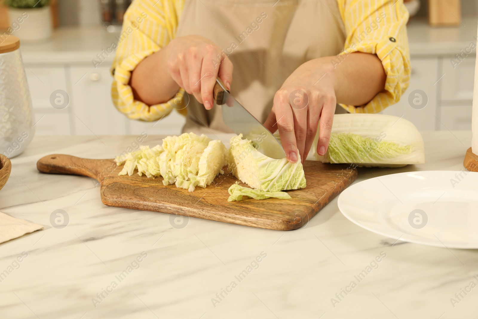 Photo of Woman cutting fresh chinese cabbage at table in kitchen, closeup