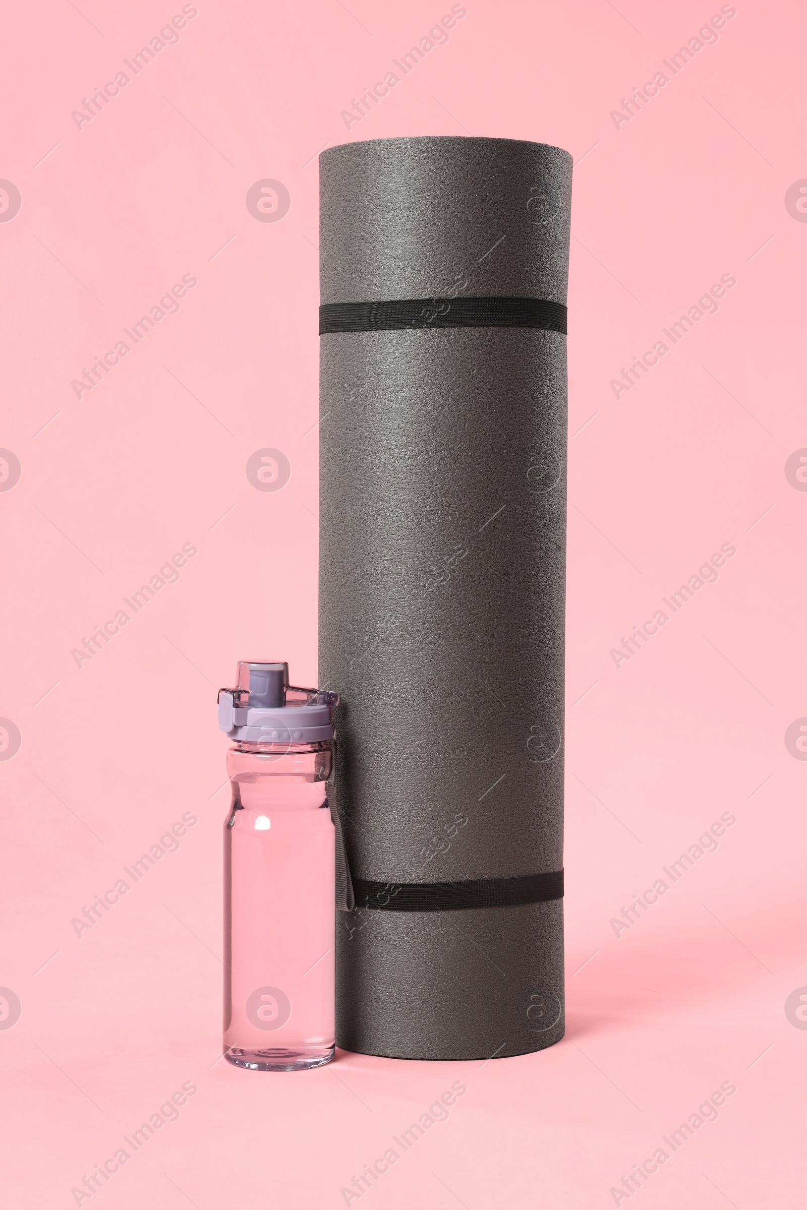 Photo of Grey yoga mat and bottle of water on pink background