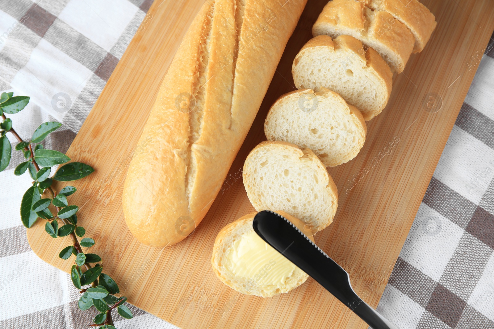 Photo of Cut baguette with fresh butter on checkered tablecloth, top view