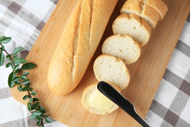 Photo of Cut baguette with fresh butter on checkered tablecloth, top view