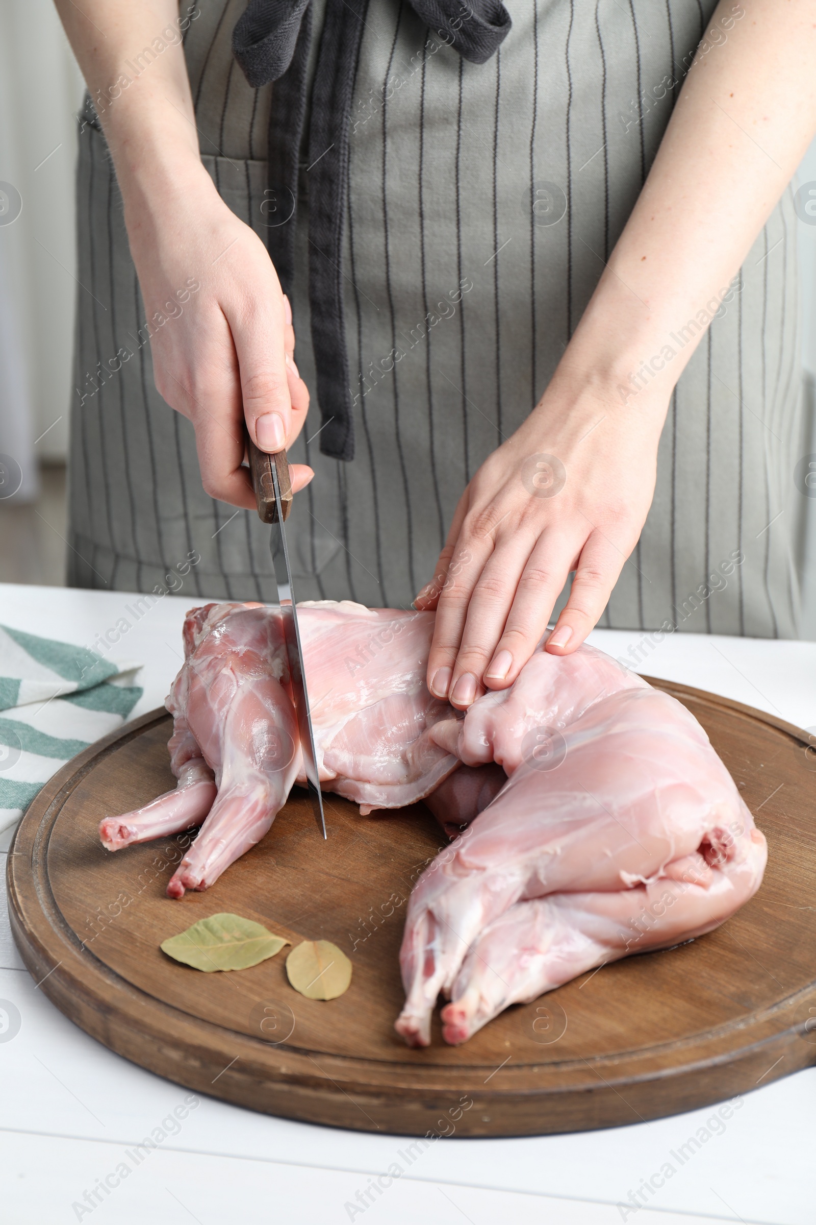 Photo of Woman cutting whole raw rabbit at white wooden table, closeup