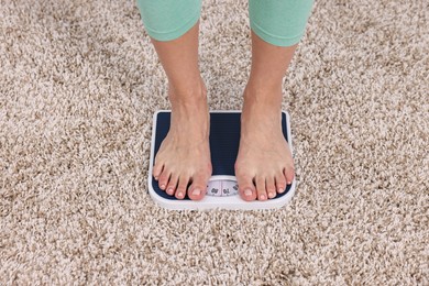 Photo of Woman standing on floor scale on carpet, closeup