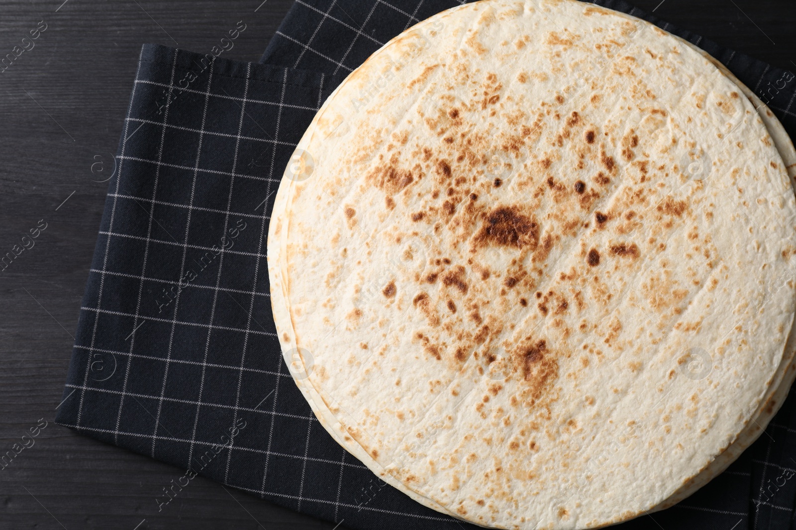 Photo of Many tasty homemade tortillas on black wooden table, top view