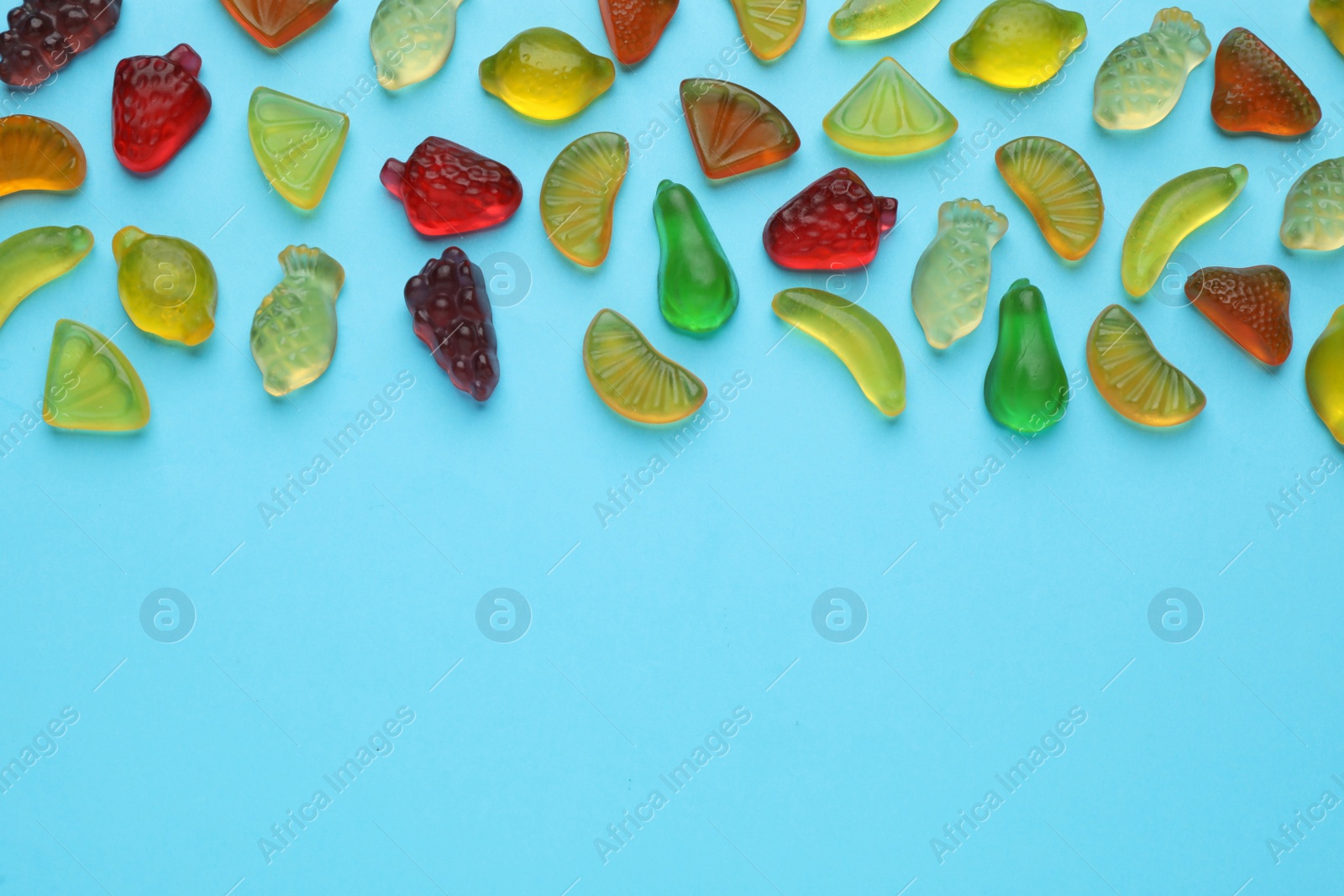 Photo of Tasty jelly candies in shape of different fruits on light blue background, flat lay. Space for text