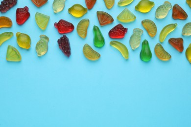 Tasty jelly candies in shape of different fruits on light blue background, flat lay. Space for text