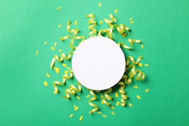 Blank card, yellow serpentine streamers and confetti on green background, flat lay. Space for text