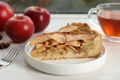 Photo of Slice of delicious apple pie served with tea on white table, closeup