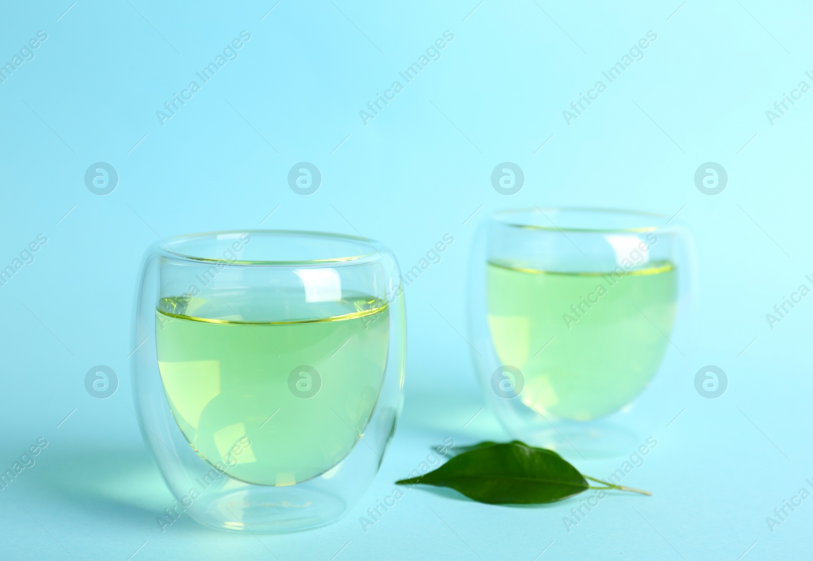 Photo of Aromatic green tea and leaves on light blue background