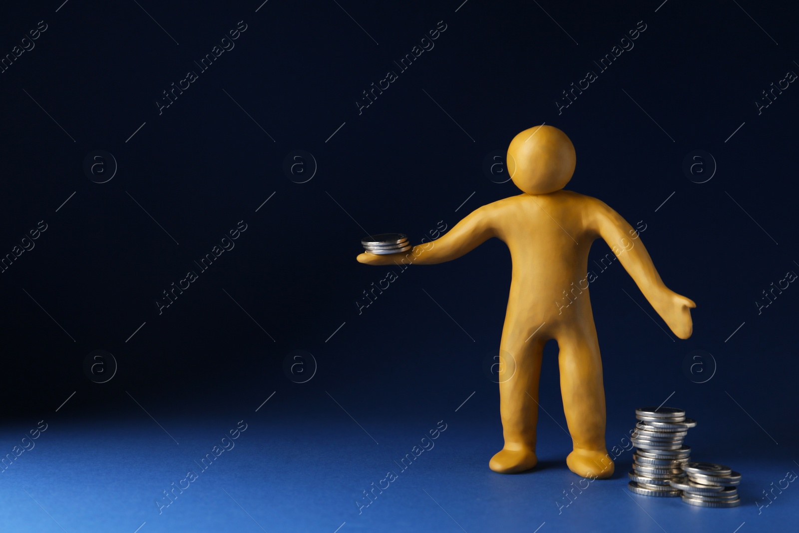 Photo of Human figure made of yellow plasticine with coins on dark blue background. Space for text