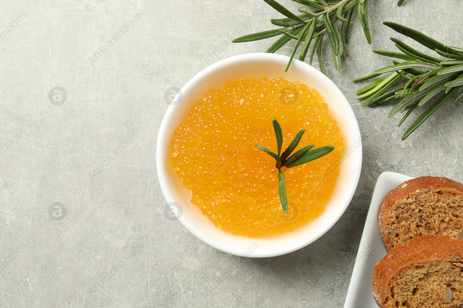 Photo of Fresh pike caviar in bowl, bread and rosemary on light grey table, top view. Space for text