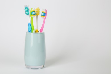 Different toothbrushes in holder on light grey background. Space for text