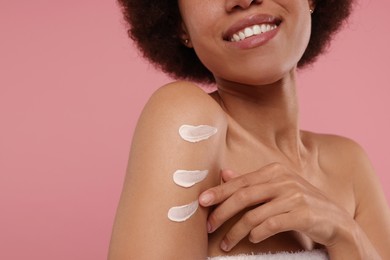 Photo of Young woman applying body cream onto arm on pink background, closeup. Space for text