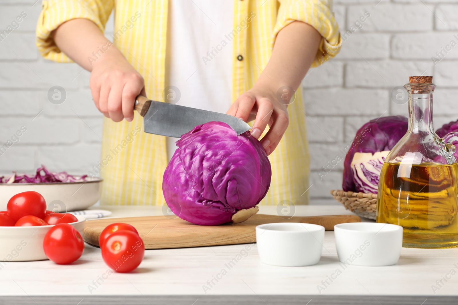 Photo of Woman cutting fresh red cabbage at white wooden table, closeup