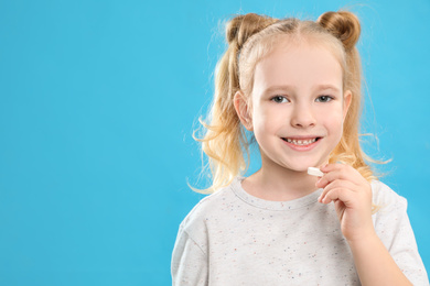 Photo of Little girl taking vitamin pill on light blue background. Space for text
