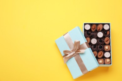 Photo of Open box of delicious chocolate candies on yellow background, flat lay. Space for text