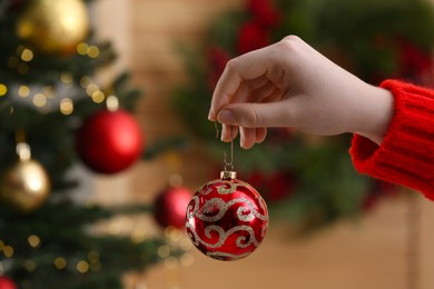 Woman holding red ball near Christmas tree indoors, closeup