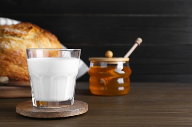 Photo of Glass with fresh milk, honey and bread on wooden table. Space for text