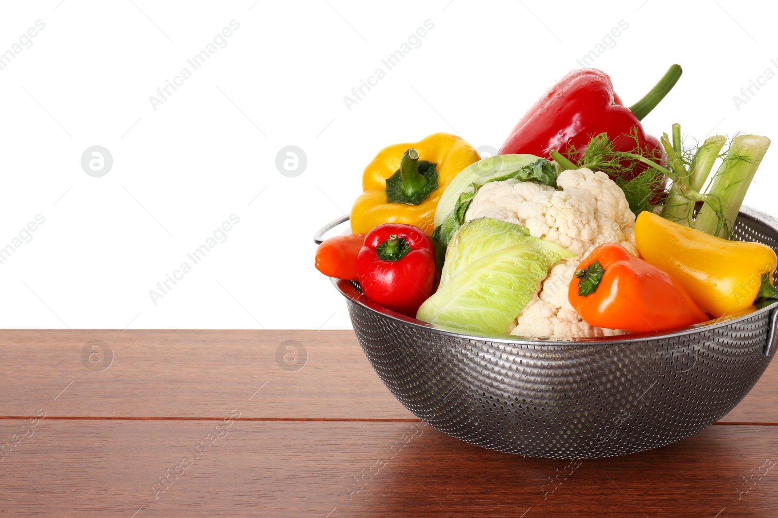 Photo of Metal colander with different vegetables on wooden table against white background, space for text