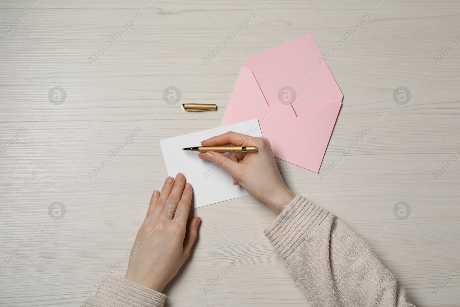 Photo of Woman writing letter at light wooden table, top view