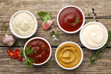 Photo of Different tasty sauces in bowls, herbs and spices on wooden table, flat lay