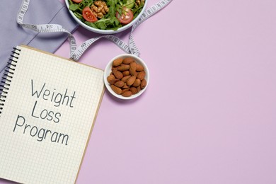 Photo of Notebook with phrase Weight Loss Program, bowl of salad and almonds on pink background, flat lay. Space for text